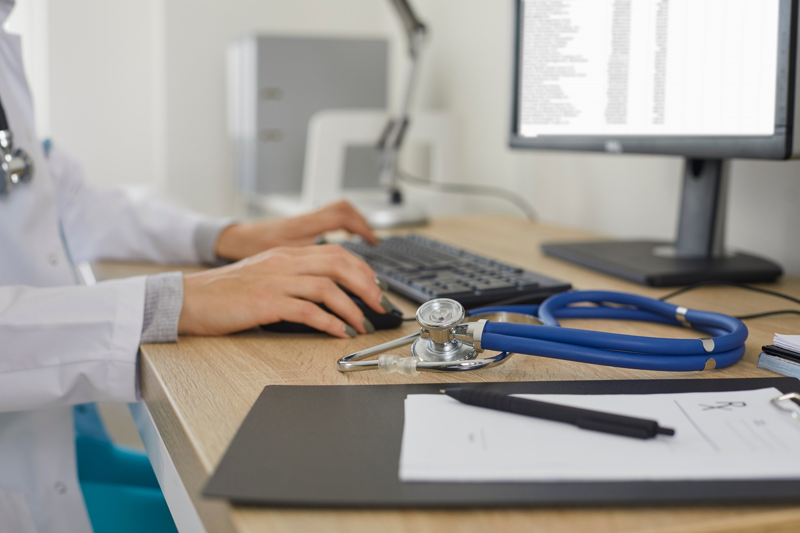 Doctor Working at Computer and Typing Electronic Medical Record Sitting near Stethoscope.